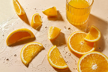 Image showing glass of juice and orange slices on wet table