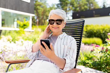 Image showing old woman with earphones and smartphone at garden