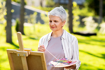 Image showing senior woman with easel painting outdoors