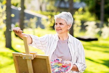 Image showing senior woman with easel painting outdoors