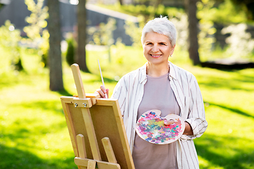 Image showing senior woman with easel painting outdoors