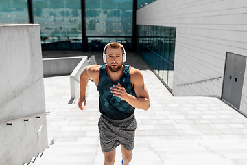 Image showing young man in headphones running upstairs outdoors