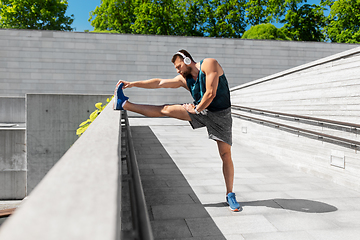 Image showing young man in headphones stretching leg outdoors