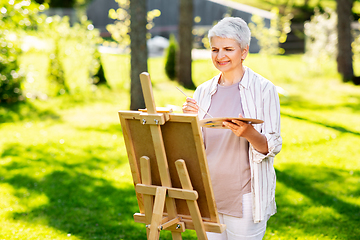 Image showing senior woman with easel painting outdoors