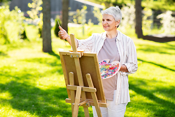 Image showing senior woman with easel painting outdoors