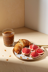 Image showing glass of coffee, croissant and grapefruit on table