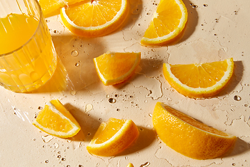 Image showing glass of juice and orange slices on wet table