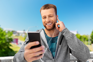 Image showing smiling young man with earphones and smartphone