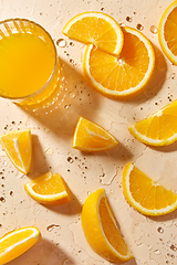 Image showing glass of juice and orange slices on wet table