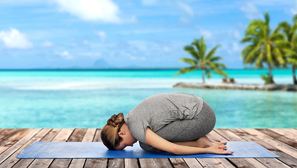 Image showing woman doing yoga child pose on mat over ocean