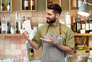 Image showing happy smiling barman in apron with bill at bar