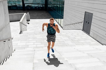 Image showing young man in headphones running upstairs outdoors