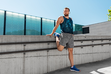 Image showing young man in headphones stretching leg outdoors