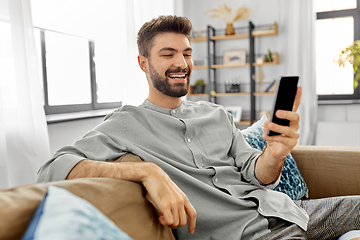 Image showing happy smiling young man with smartphone at home