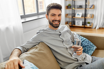 Image showing happy man drinking water from glass bottle at home