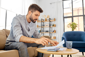 Image showing man with bills counting on calculator at home