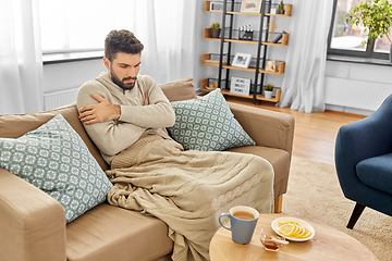 Image showing sick young man in blanket drinking hot tea at home