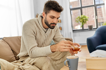 Image showing sick young man in blanket drinking hot tea at home