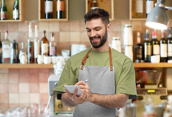 Image showing smiling waiter in apron taking notes to notepad