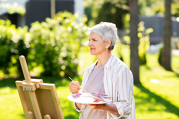 Image showing senior woman with easel painting outdoors