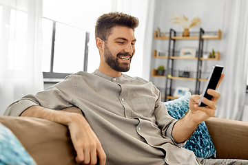 Image showing happy smiling young man with smartphone at home