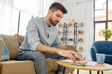 Image showing man with bills counting on calculator at home