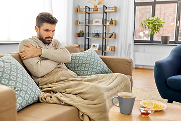 Image showing sick young man in blanket drinking hot tea at home