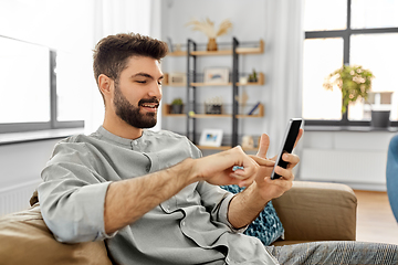 Image showing happy smiling young man with smartphone at home