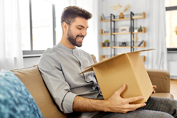 Image showing happy smiling man opening parcel box at home