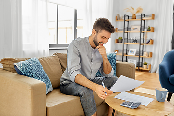 Image showing man with bills counting on calculator at home