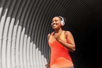 Image showing happy african woman in headphones running outdoors