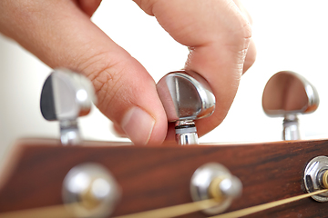 Image showing close up of hand tuning guitar strings with pegs