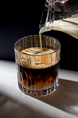 Image showing hand with jug pouring cream to glass of coffee