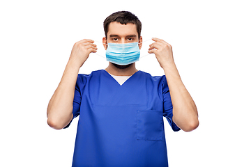 Image showing male doctor in blue uniform putting on mask