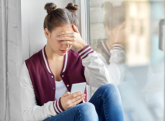 Image showing teenage girl with smartphone sitting on windowsill