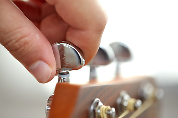 Image showing close up of hand tuning guitar strings with pegs