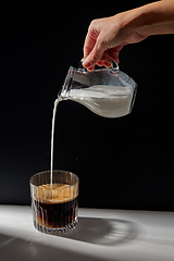 Image showing hand with jug pouring cream to glass of coffee