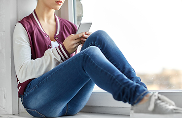 Image showing teenage girl with smartphone sitting on windowsill