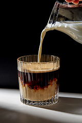 Image showing hand with jug pouring cream to glass of coffee