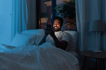 Image showing indian man with smartphone in bed at home at night