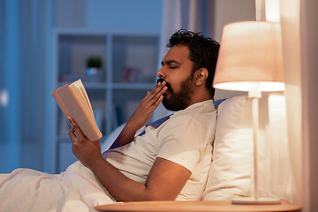 Image showing yawning indian man reading book in bed at night