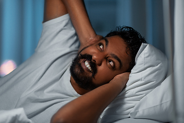 Image showing annoyed indian man lying in bed and closing ears