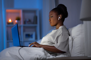 Image showing woman with laptop and earphones in bed at night