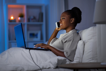 Image showing woman with laptop calling on smartphone in bed