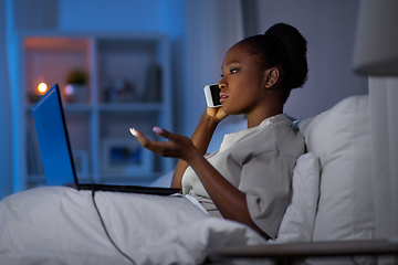 Image showing woman with laptop calling on smartphone in bed