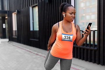 Image showing female marathon runner with smartphone stretching