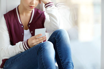 Image showing teenage girl with smartphone sitting on windowsill