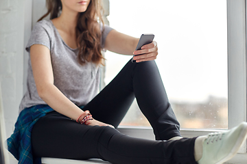 Image showing teenage girl with smartphone sitting on windowsill