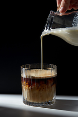 Image showing hand with jug pouring cream to glass of coffee