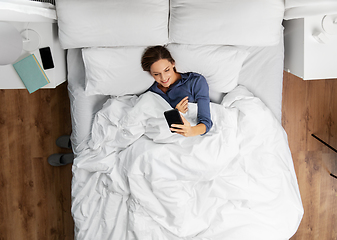 Image showing young woman with smartphone lying in bed